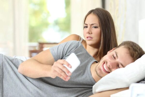 a man looking at his phone with his upset girlfriend beside him